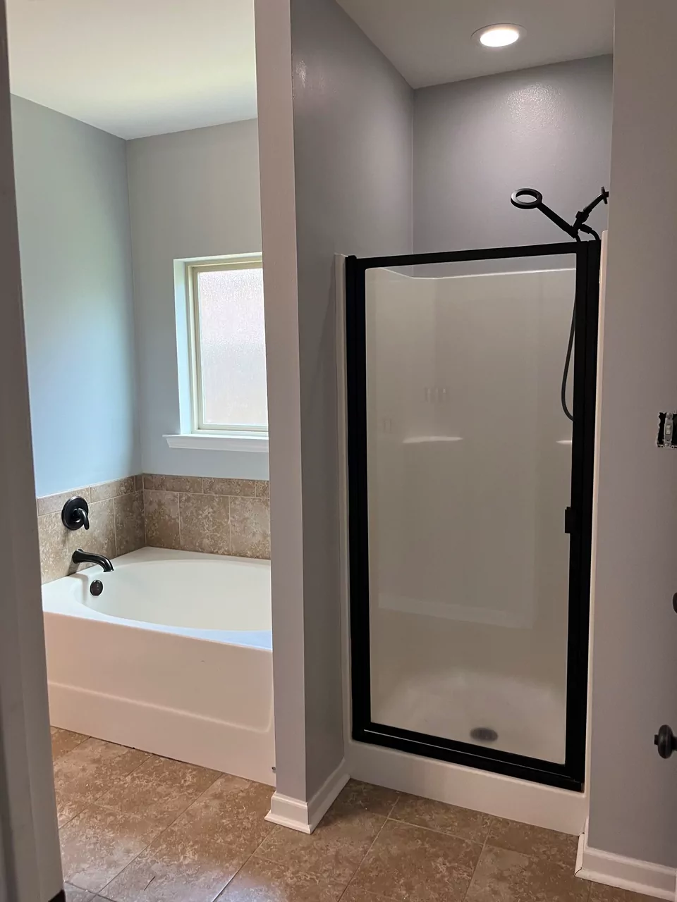 A finished bathroom: grey walls, a tiled soaking tub surround under a window, and a black-framed shower enclosure.