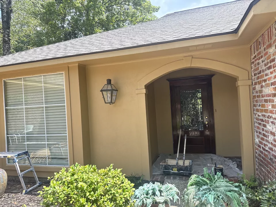 The arched front entry of a house with brick and stucco walls, a carriage lantern and a ladder and painting equipment set up at the door.